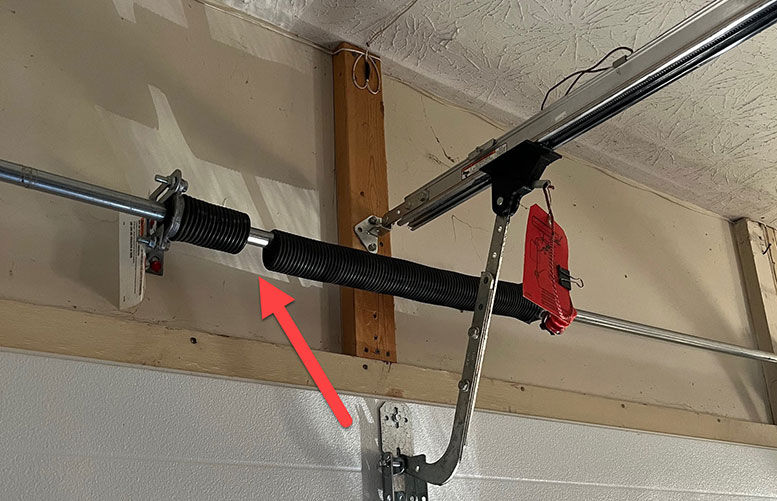 Garage door torsion spring for repair, highlighted by arrow