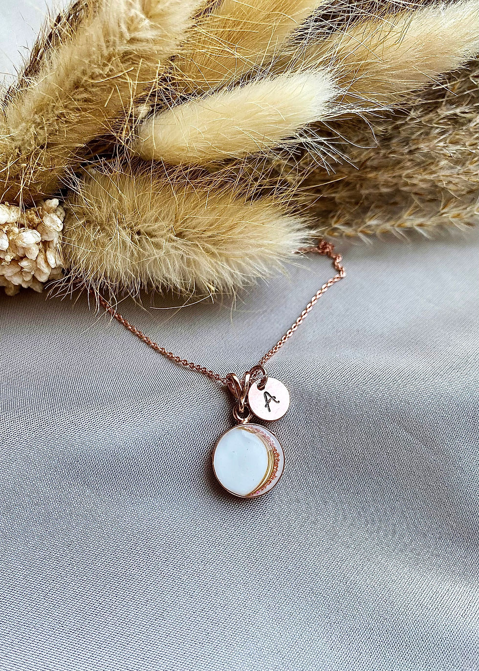 Moedermelkjuweel en/of haarlokjuweel, waarin subtiel gebogen haartjes verwerkt zijn. Het juweel is versierd met parelmoer, bl