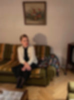 Danish illustrator and actress Liv Hansen seated in a retro Danish living room with vintage furniture and floral painting.