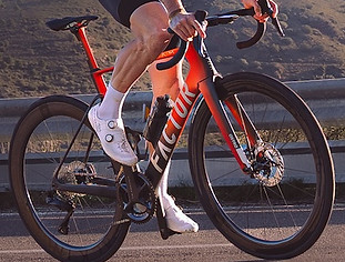Factor Ostro VAM aero road bike in terracotta red and black, ridden on a coastal road
