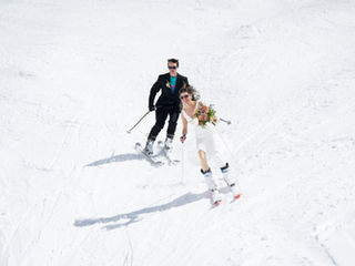 Bride and groom skiing down a groomed run together in wedding attire, bride holding her bouquet