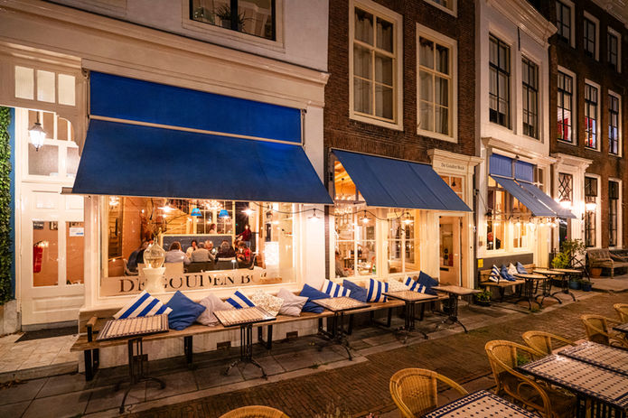 De Gouden Bock visrestaurant in Middelburg met blauwe zonneschermen en sfeervol verlicht winterterras aan het Damplein.