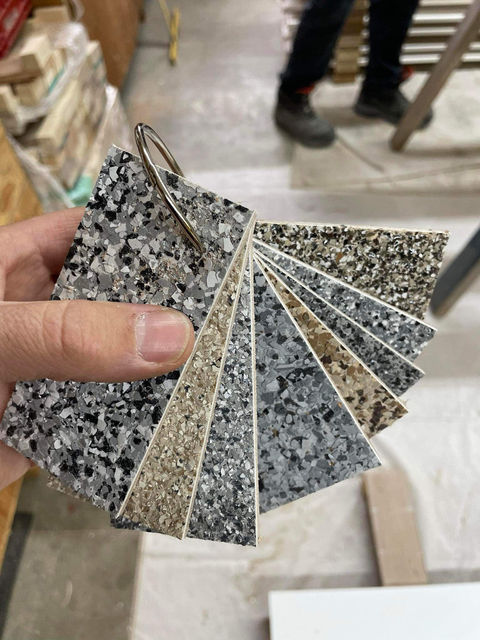 Hand holding a fan of eight topcoat colour samples, each with a speckled pattern.