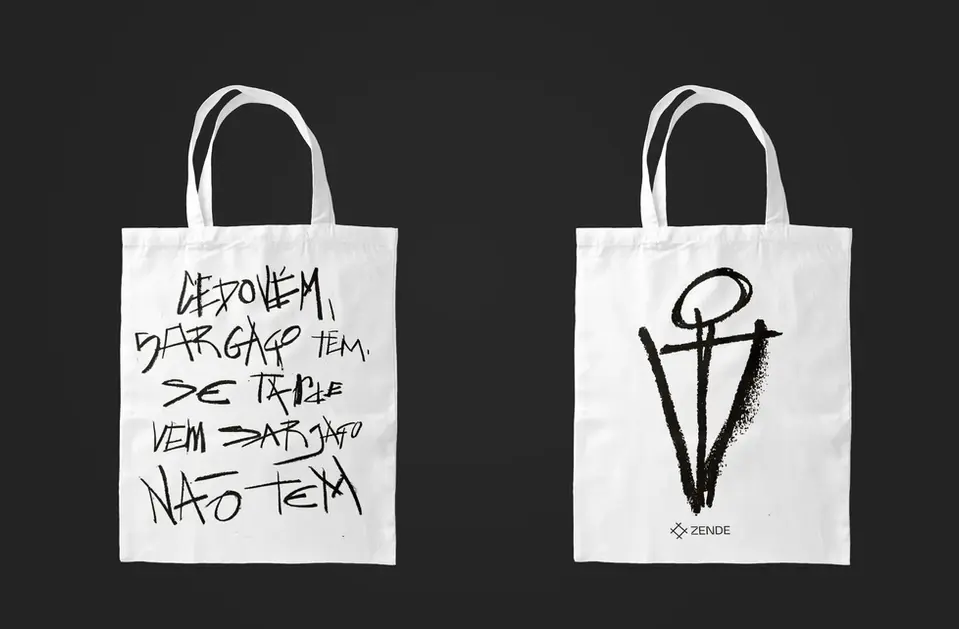 Two white tote bags with black graphic designs—one with graffiti-style text, the other with an abstract symbol and “ZENDE” branding.
