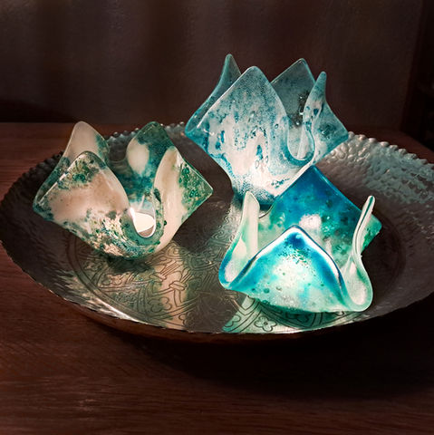 De theelichten van gesmolten glas op een marokkaans dienblad. De theelichten zijn in aquablauw, ijsblauw, creme-wit en smaragd groene tinten. In de windlichtjes branden kaarsjes wat een magisch effect heeft.