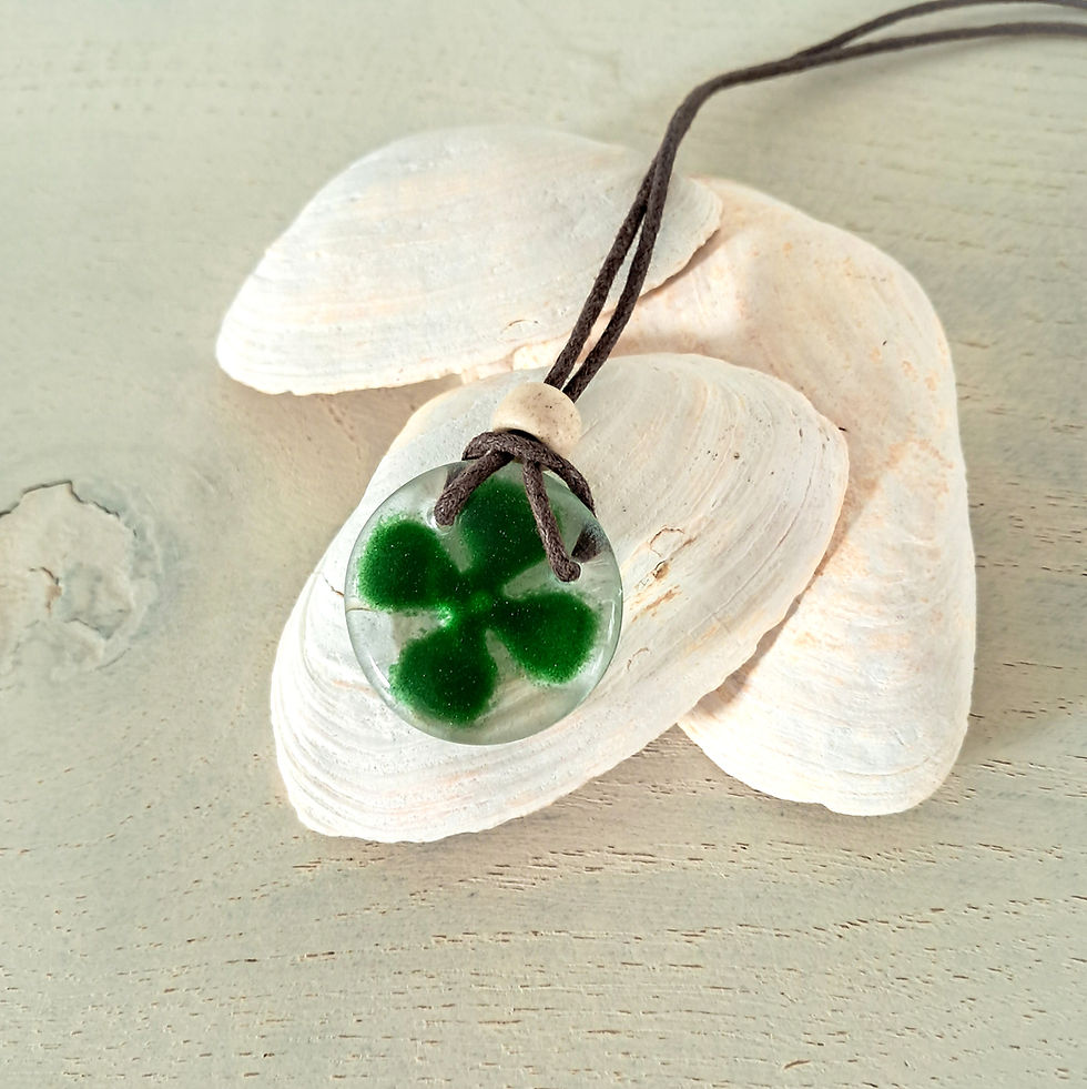 Hanger van gesmolten glas met een groen klavertje vier in het glas, de glazen hanger zit aan een bruin waxkoord.