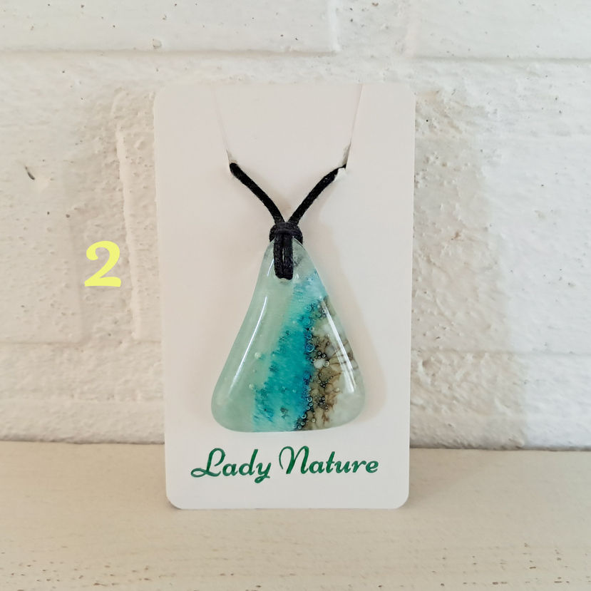 Thumbnail: Glazen hanger met een aquablauw zeegezicht. De hanger van gefuseerd glas hangt aan een zwart waxkoord.