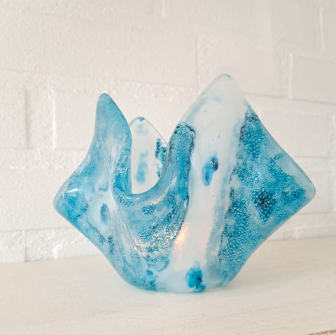 Glaskunst theelicht van gesmolten glas in aqua blauw, ijsblauw en witte tinten. Er zitten golfbewegingen en luchtbellen in het glas. Het doet denken aan zee, zeegezicht.