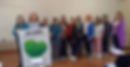 Grupo de mulheres da equipe Quem Somos ao lado de banner da Bio-Saúde.