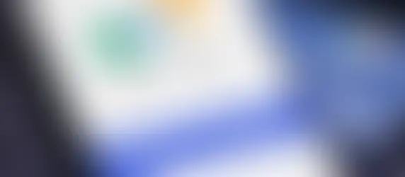 Em uma tela de celular, está a logo do aplicativo MEU INSS, com cartão do INSS de fundo e teclado do computador por baixo