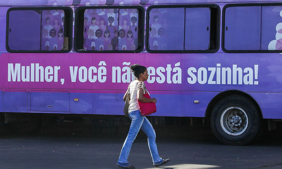 mulher no centro da foto passando em frente a um ônibus com a frase lateral: mulher, você não está sozinha