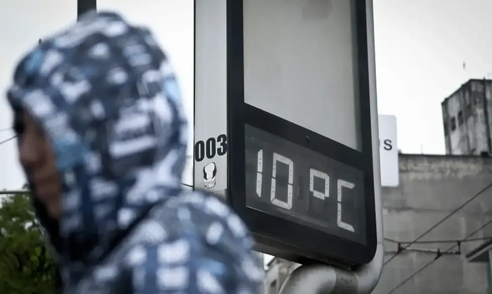 pessoa encapuzada com termômetro de rua marcando dez graus celsius