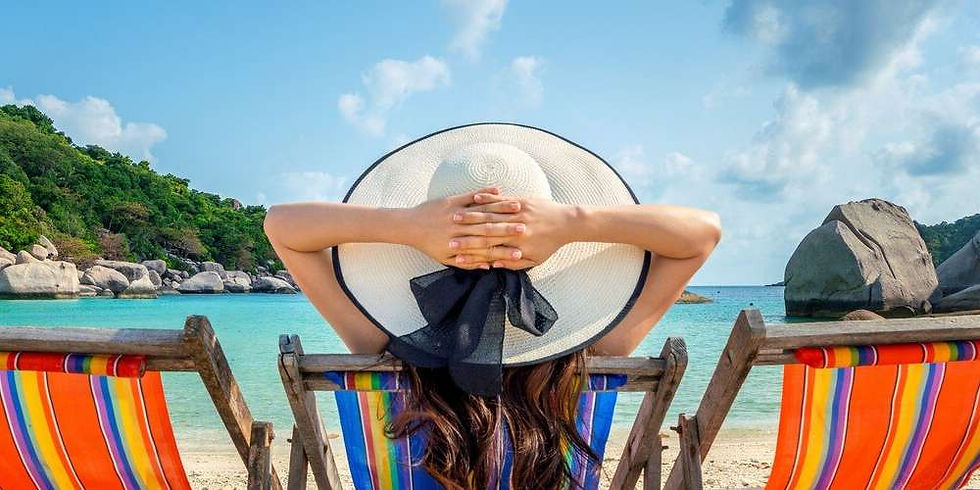 Mulher de costas com chapéu grande de praia sentada em uma cadeira colorida com as mãos entrelaçadas na cabeça. Ela está contemplando o mar cor de jade em meio a uma praia ensolarada