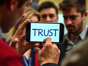 Man holding a iPhone with the word TRUST on the screen.