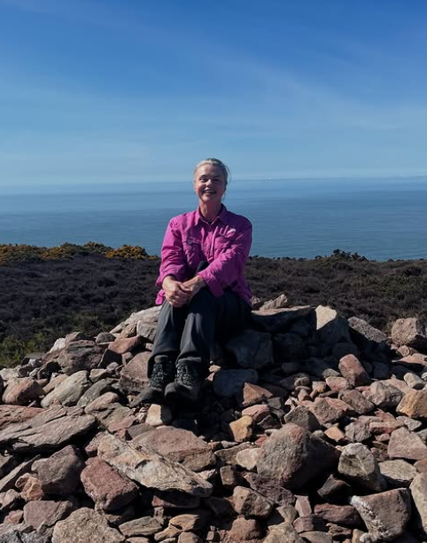Relishing a tranquil moment, Katy relaxes on a rocky ledge with a breathtaking coastal view behind her.