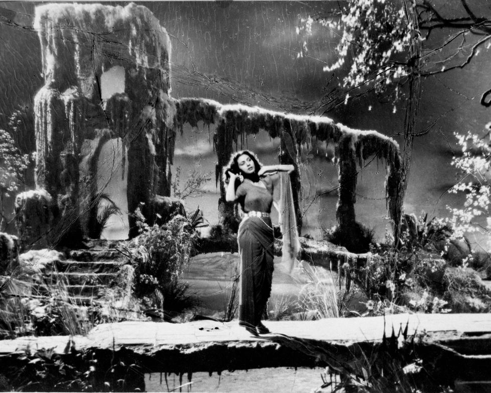 a black and white photo of a woman standing on a bridge