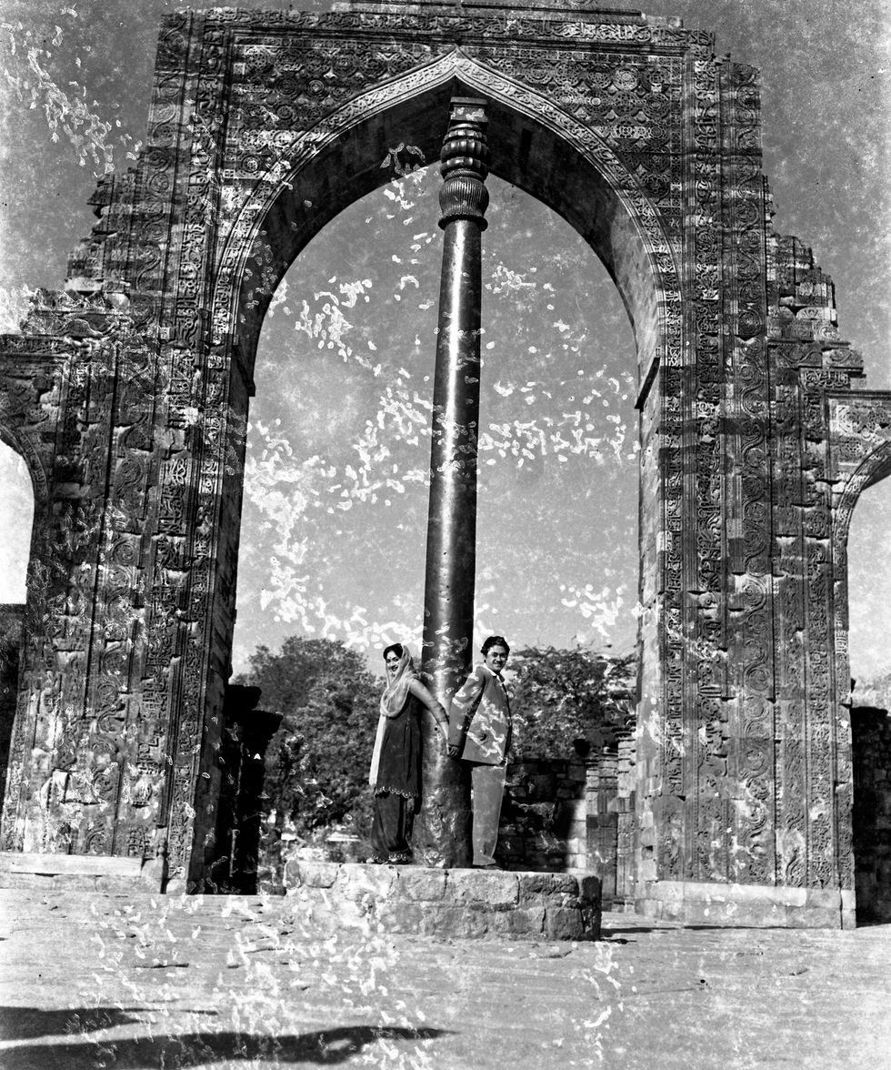 a black and white photo of two people standing in front of a stone archway