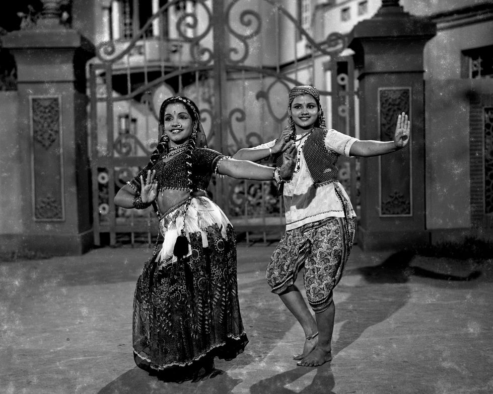 two women are dancing in front of a wrought iron gate