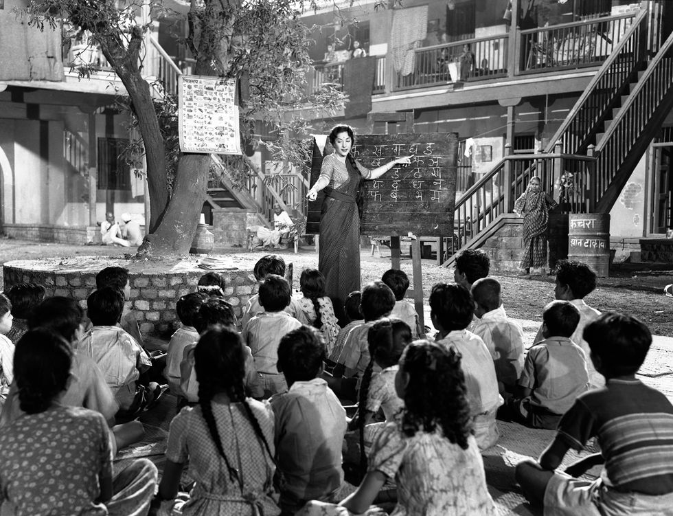 a black and white photo of a woman teaching a group of children