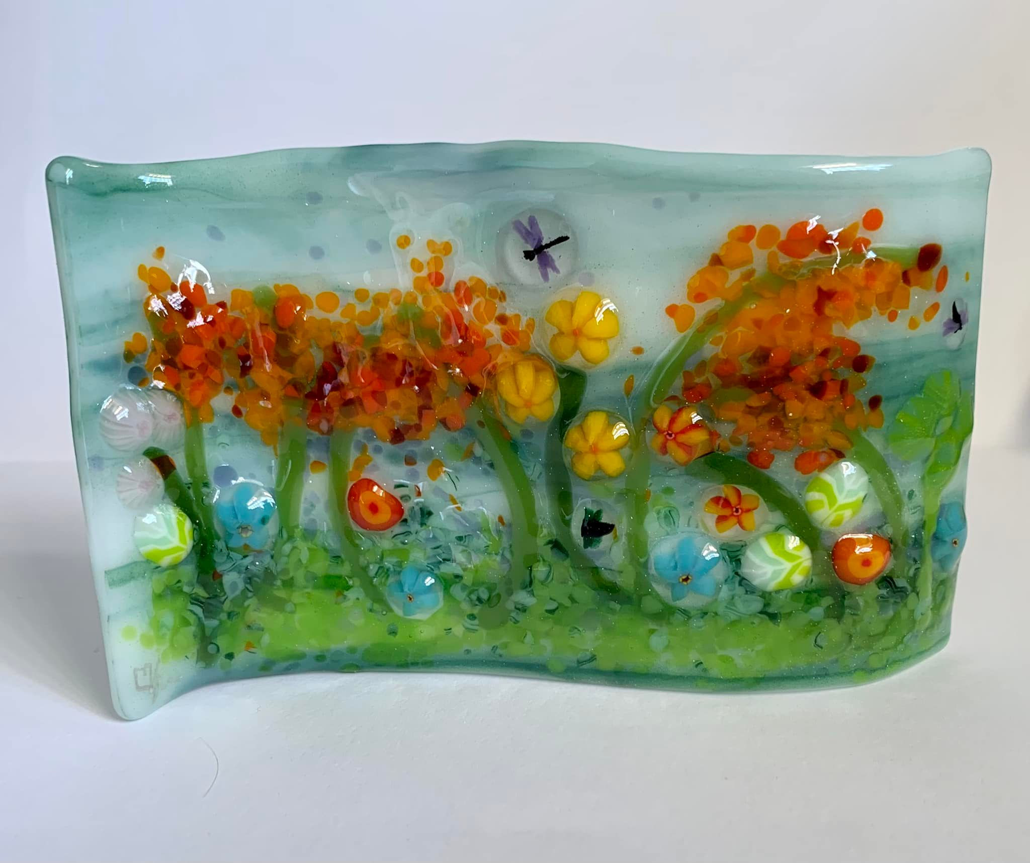 Textured Fused glass art piece depicting Wildflowers on a green and white background.  Slumped into an S-Curve to be self standing.