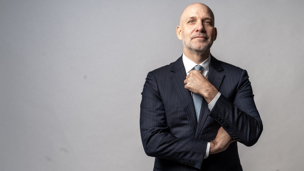 Man in pinstripe suit adjusting his tie against grey backdrop, photographed by Aemilia Cumberland