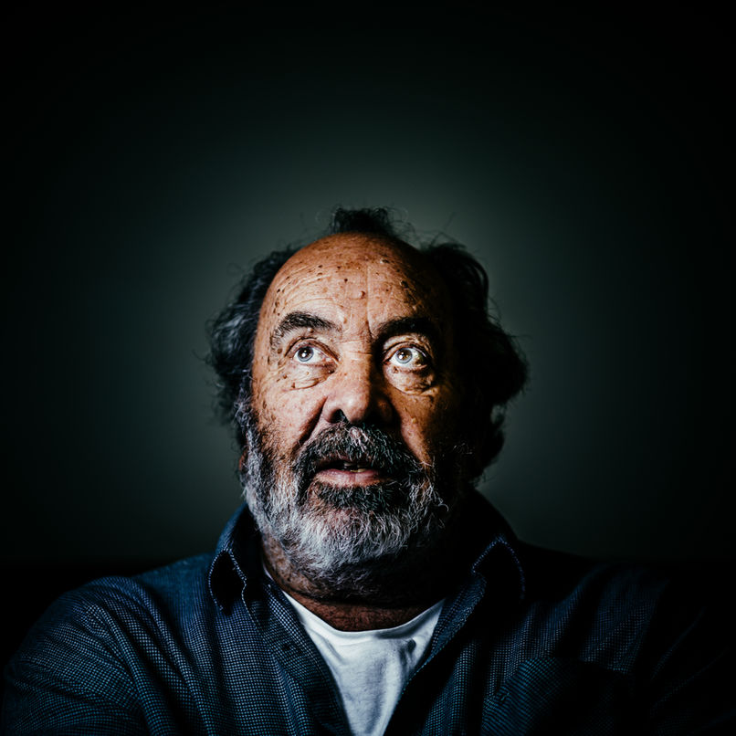 Bearded man with curly hair gazing upward, lit dramatically against dark background, photographed by Aemilia Cumberland