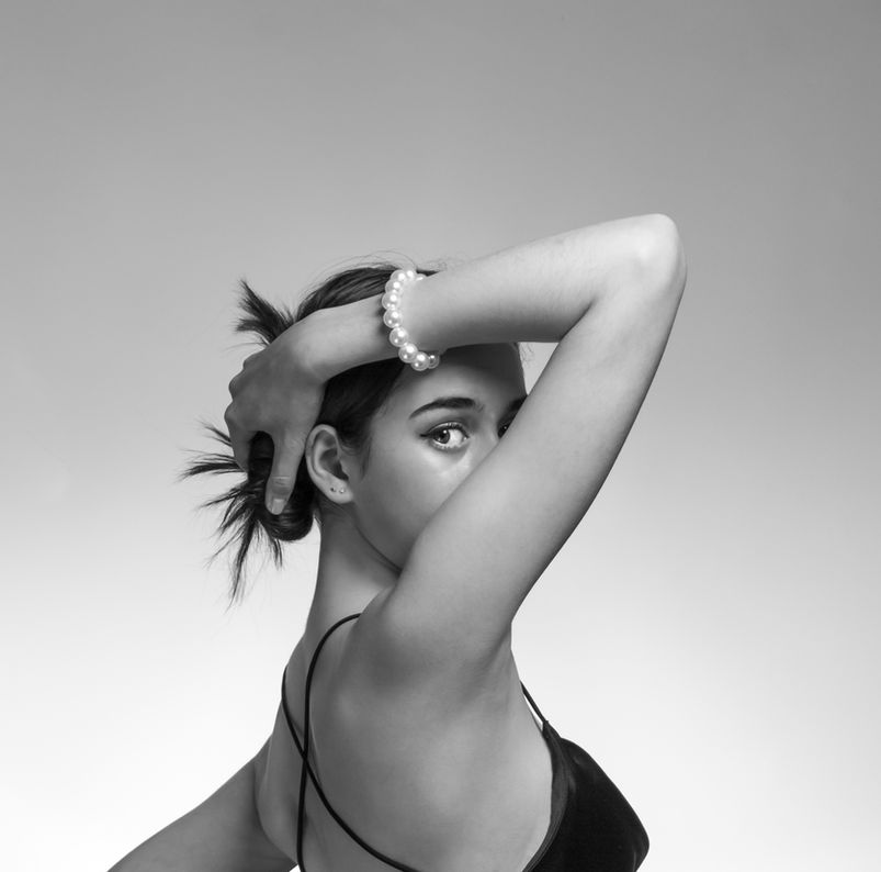 Woman with hair tied up wearing pearl bracelet and dark top against neutral background, photographed by Aemilia Cumberland