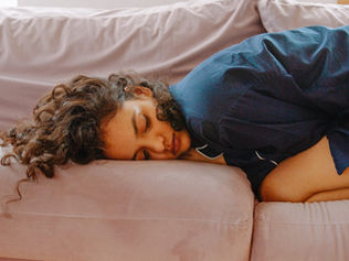 A woman curled up in pain from her menstrual cycle  on a pink couch