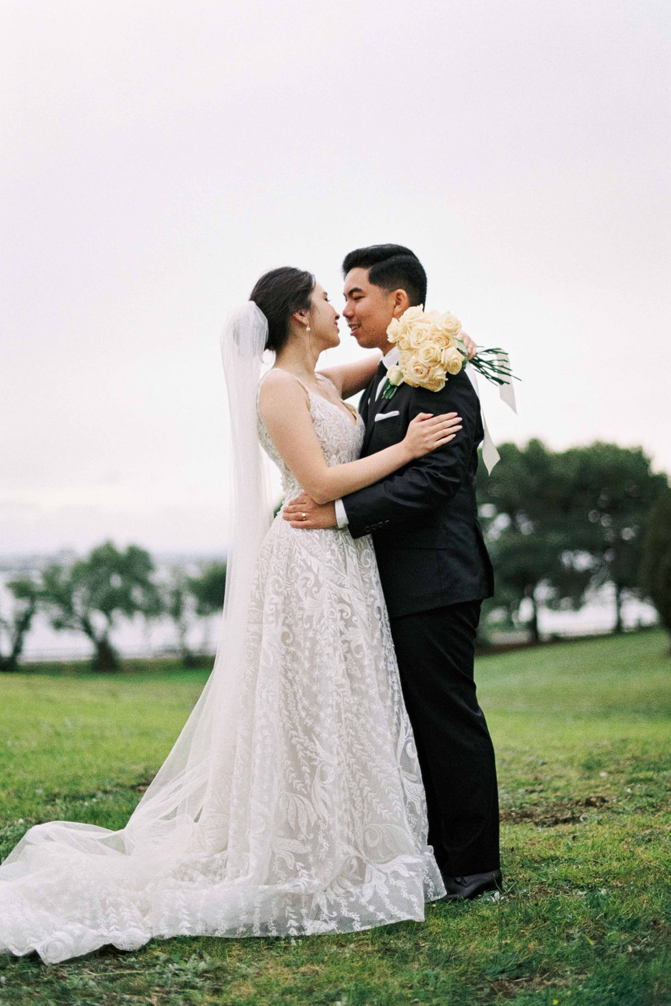 a bride and groom kissing in a field with trees in the background