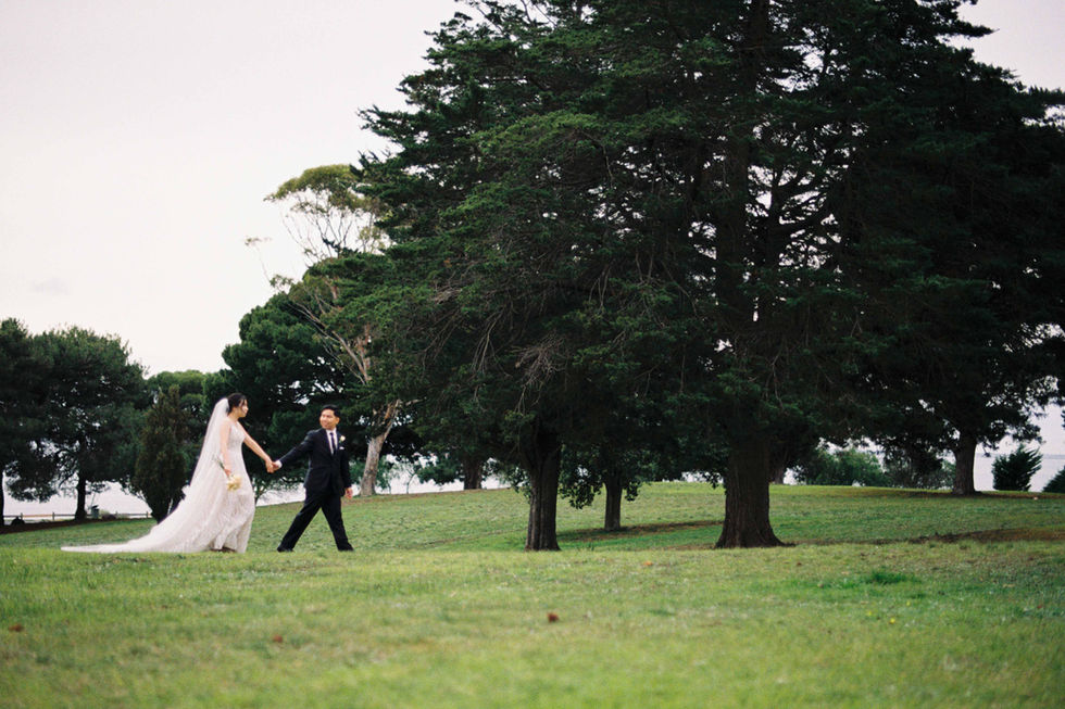 a bride and groom are walking in a field holding hands