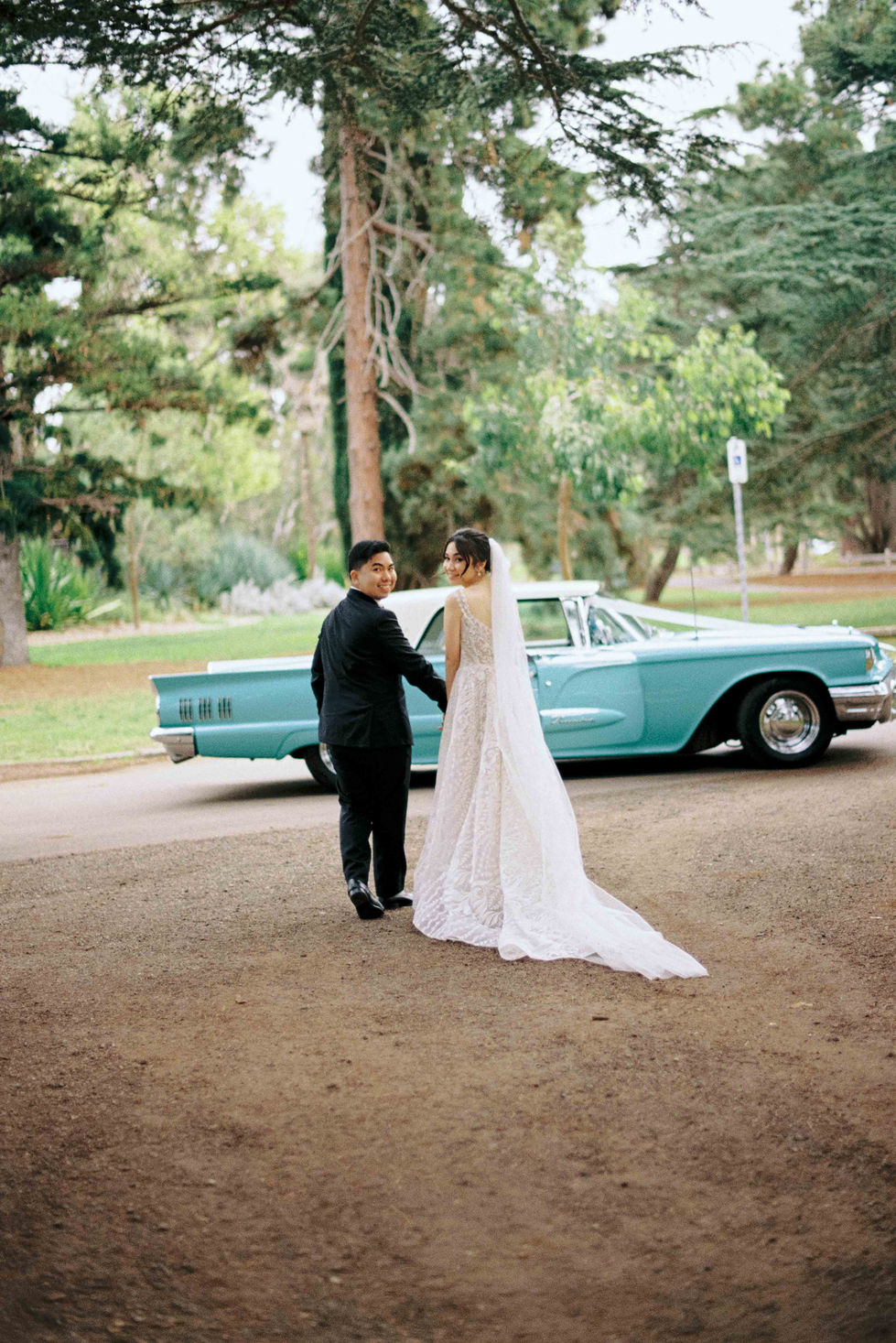 a bride and groom standing in front of a blue car