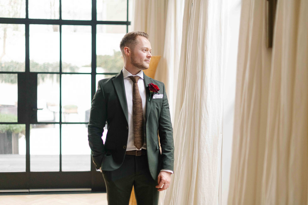 a man in a green suit and brown tie stands in front of a window
