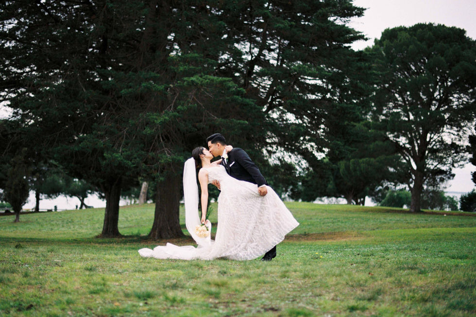 a bride and groom kissing in a field with trees in the background