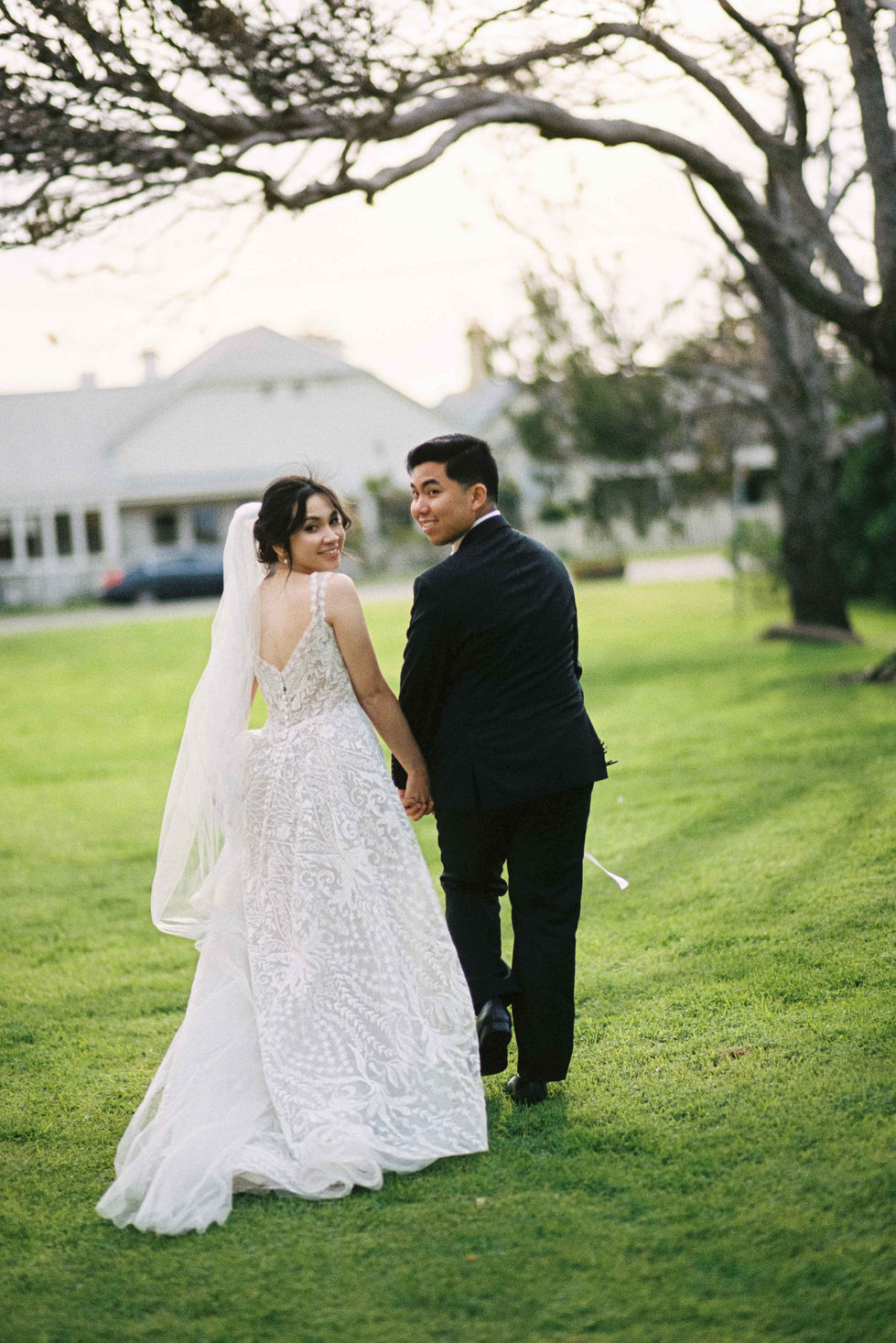 a bride and groom are walking in the grass holding hands