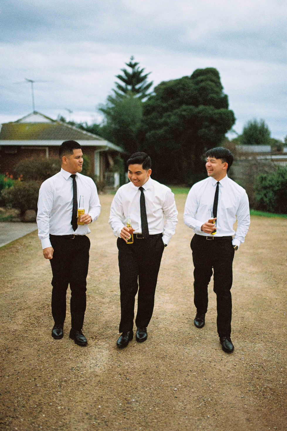 three men in white shirts and black ties are walking down a dirt road