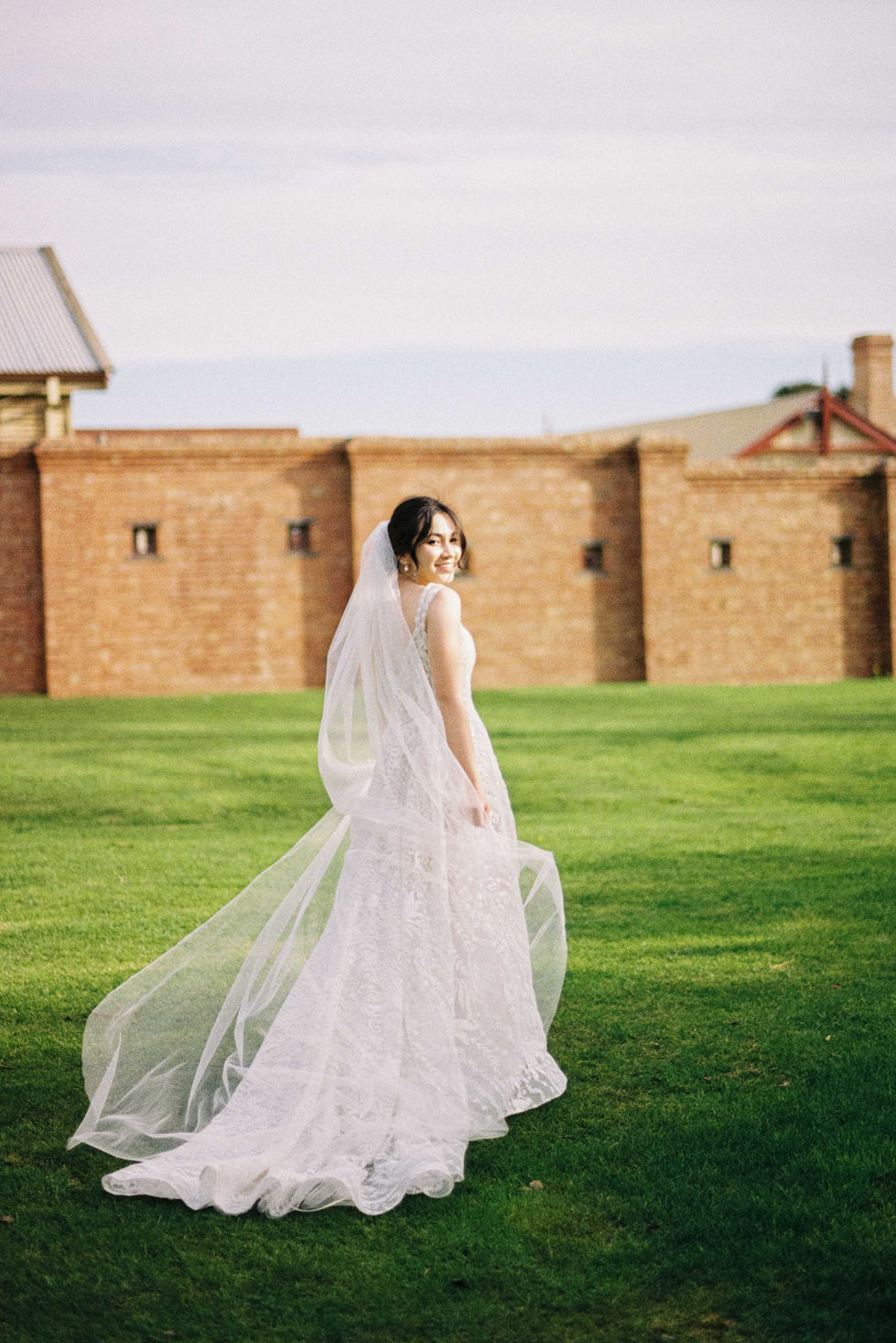 a woman in a wedding dress and veil stands in front of a brick wall