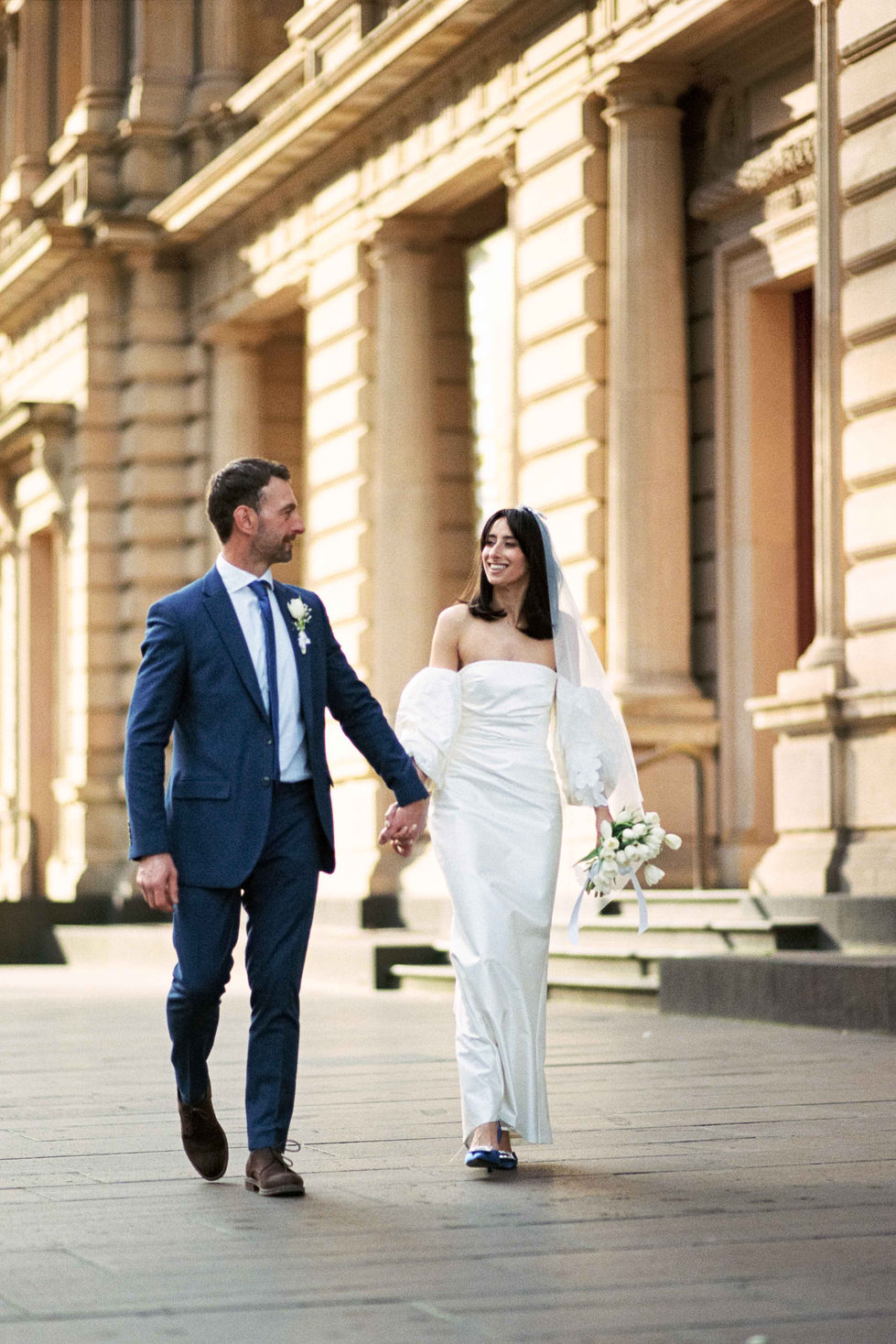 a bride and groom are walking down the street holding hands
