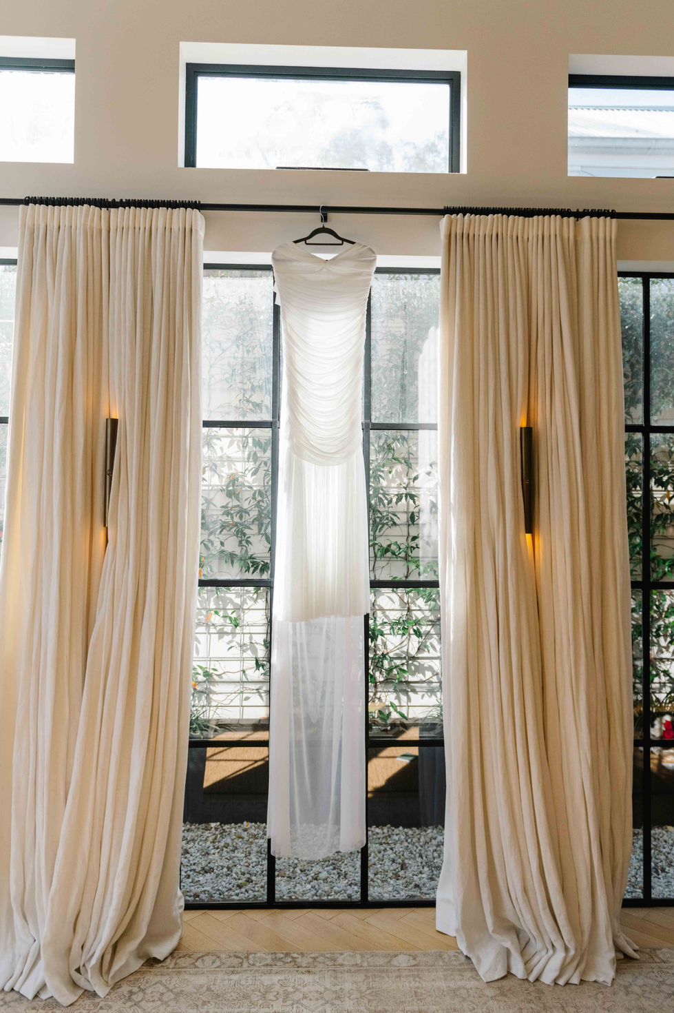 a white dress hangs on a hanger in front of a window