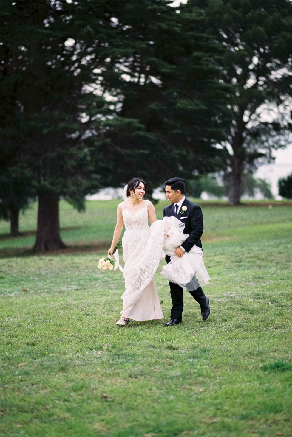 a bride and groom are walking through a grassy field