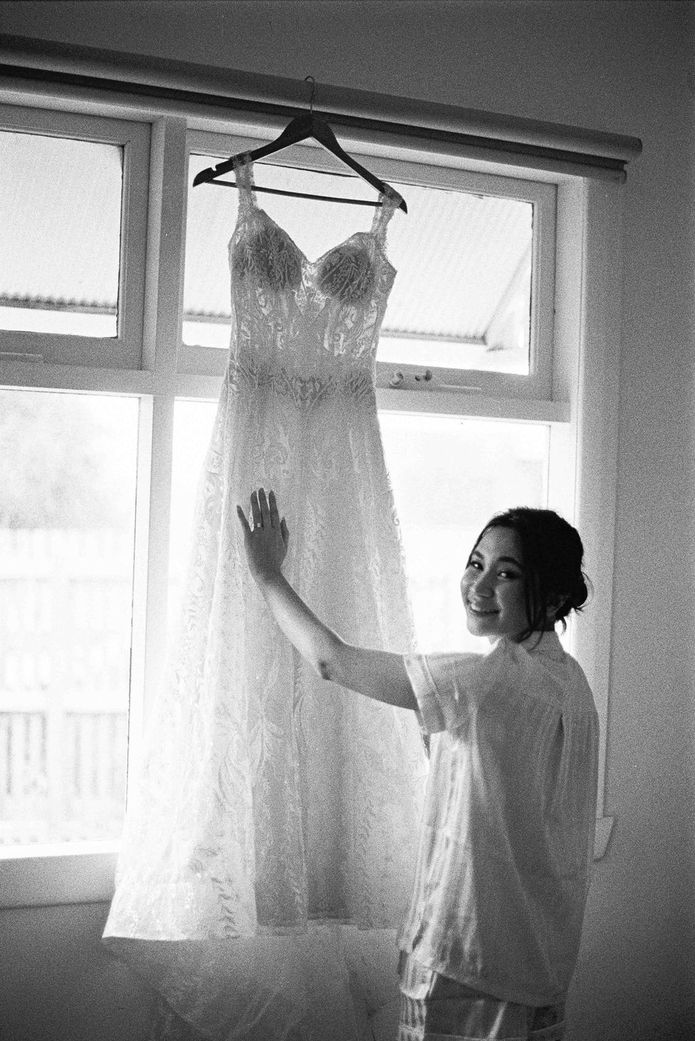 a woman holds up a wedding dress in front of a window