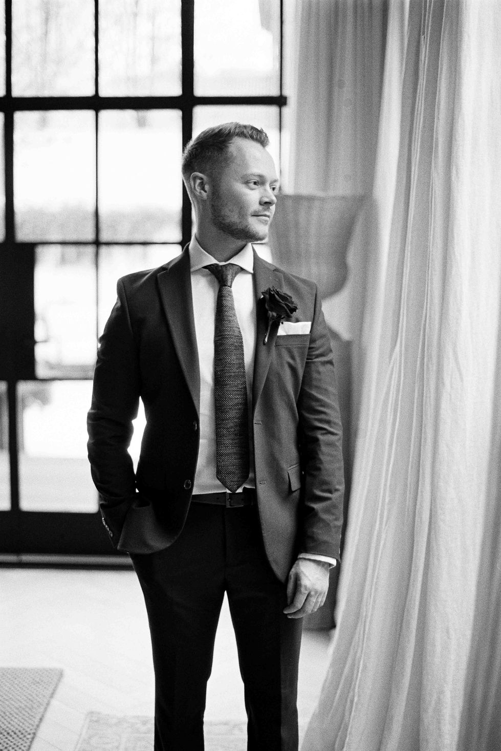 a man in a suit and tie stands in front of a window