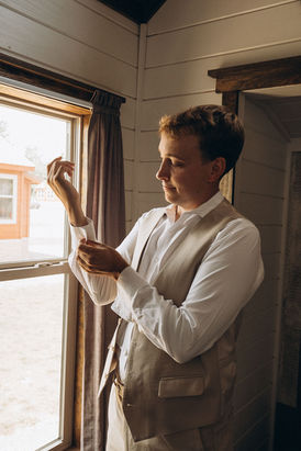 Man adjusting cufflink, wearing a vest, preparing for wedding, window background, wedding photography Chicago.
