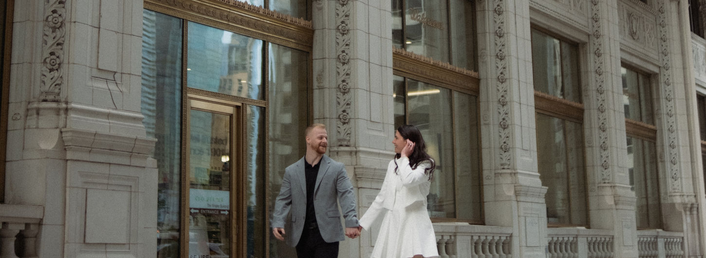 Couple walking, holding hands, smiling near a building, engagement photography