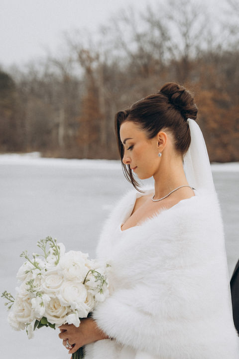 Jessica, the bride, in white fur stole with bouquet in winter