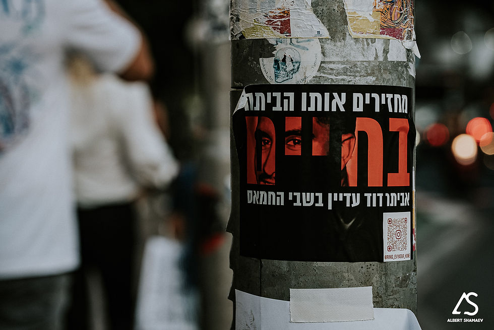 “Hebrew poster ‘בחיים’ demanding hostage return pasted on Tel Aviv pole, night bokeh”