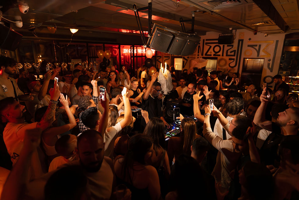 Packed nightclub dance floor surrounding DJ booth as performer leads crowd with raised phones