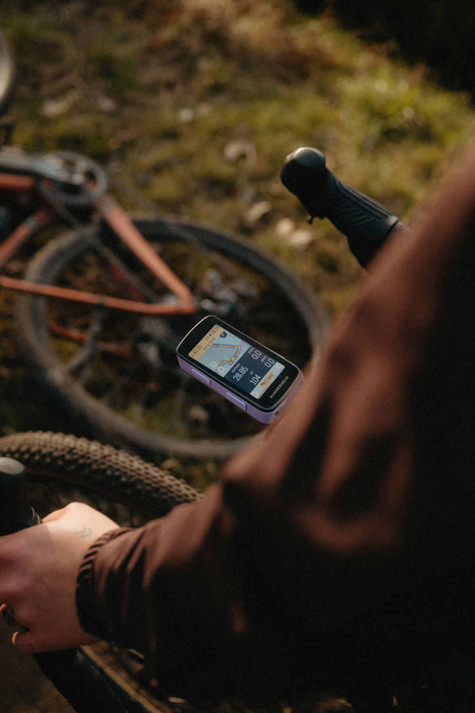 Over-shoulder view of cyclist holding Hammerhead Karoo with lavender Elevation Series shell, screen showing route map, gravel bike in background
