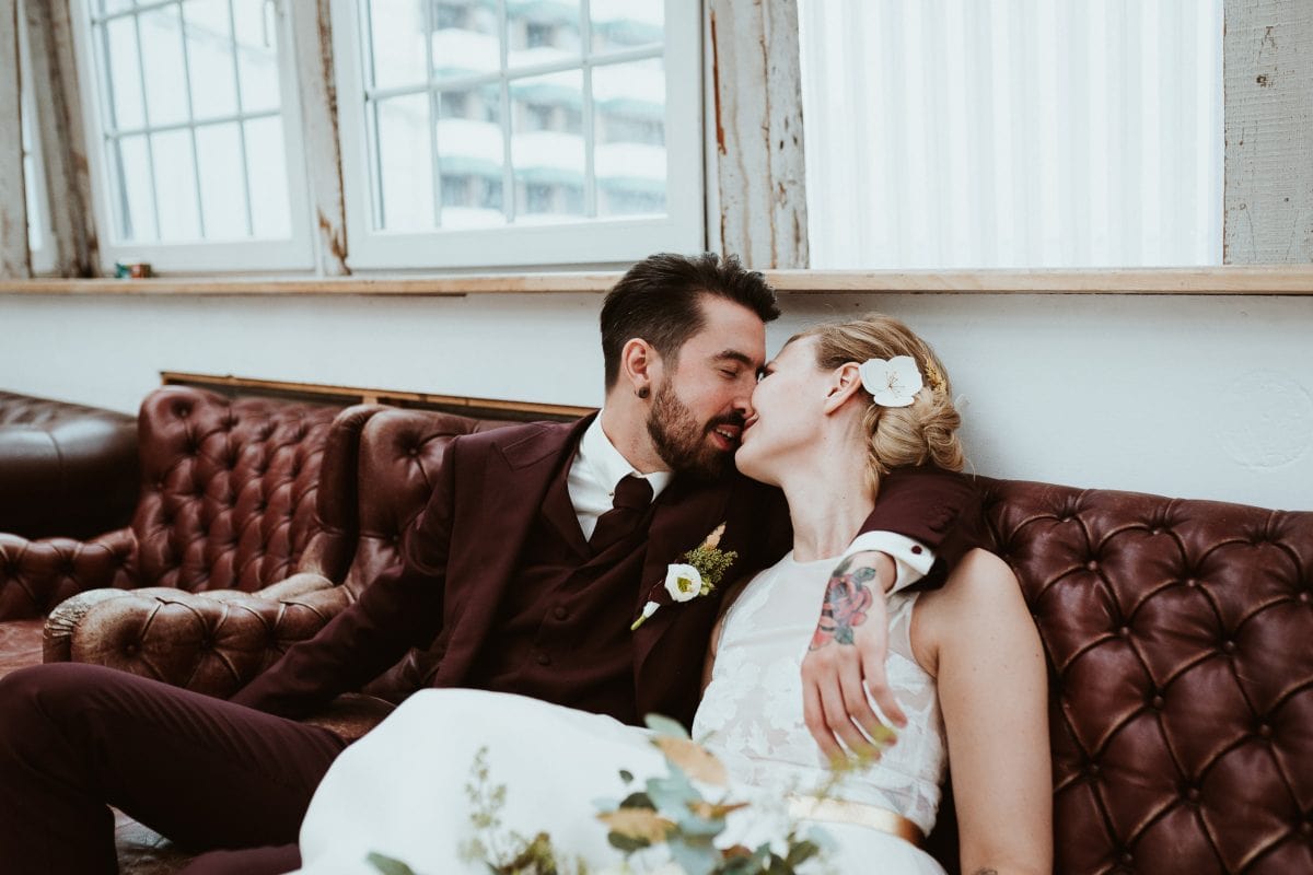 Reasons to elope: to make a statement about societal norms, like this couple kissing on a leather couch inside a huge photo studio which they rented out for their elopement. The groom has a tattoo on hand.