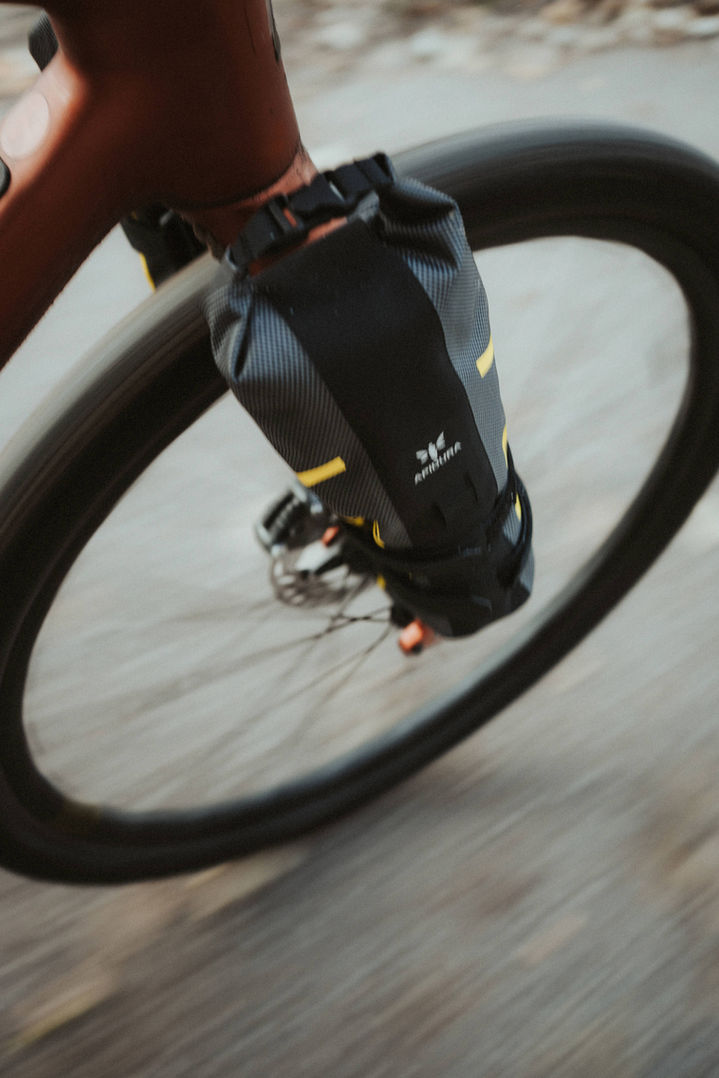 Motion blur shot of Apidura cargo cage pack under spinning rear wheel of orange gravel bike while riding, Hamburg Elbe area, December 2022`