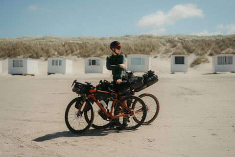 Two loaded bikepacking bikes on a wide sandy beach with white beach huts in the background, blue sky, Vestkystruten, Danish coast, 2022